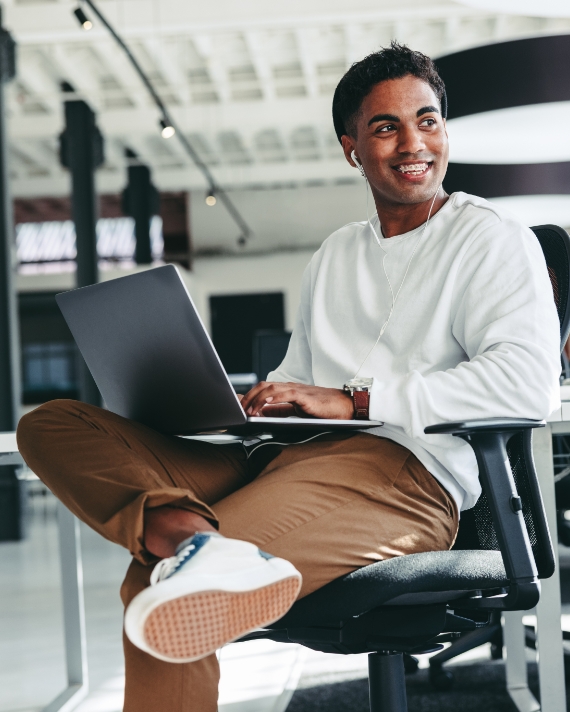 man in an office holding an open laptop smiles off camera